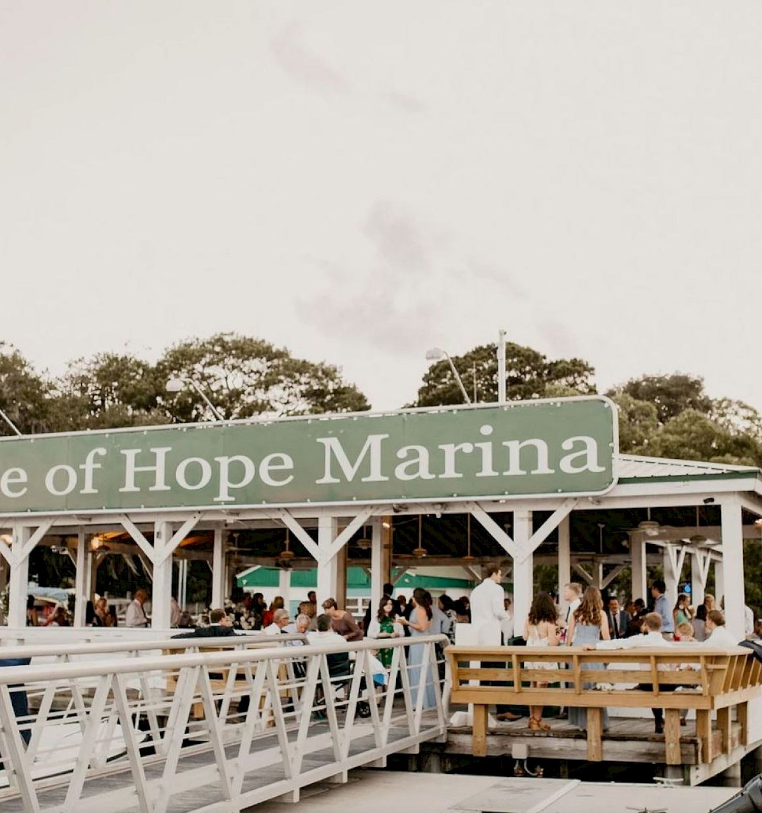 This image shows the Isle of Hope Marina with people gathered under a covered area. Nearby, there is water and a wooden dock area.