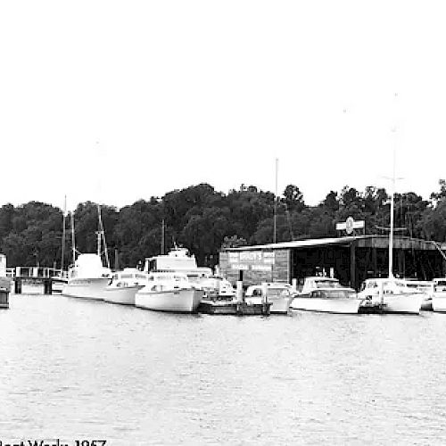 This image shows several boats docked at a marina with a large building labeled 