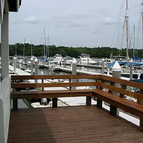 A wooden deck overlooks a marina filled with various docked boats, surrounded by a serene waterside environment.