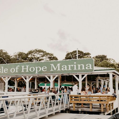 The image shows the Isle of Hope Marina with a gathering of people under a pavilion near the water, surrounded by trees and houses.