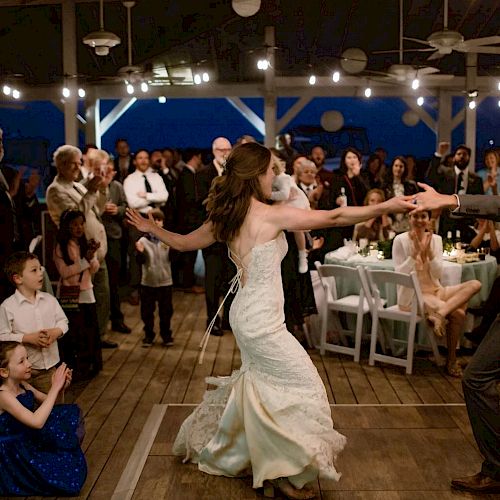 A couple dances in the center of a crowded celebration, surrounded by guests who are watching and clapping in a warmly lit festive atmosphere.