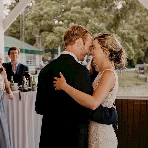 A couple shares a dance at an outdoor event, while other guests chat and enjoy drinks in the background.