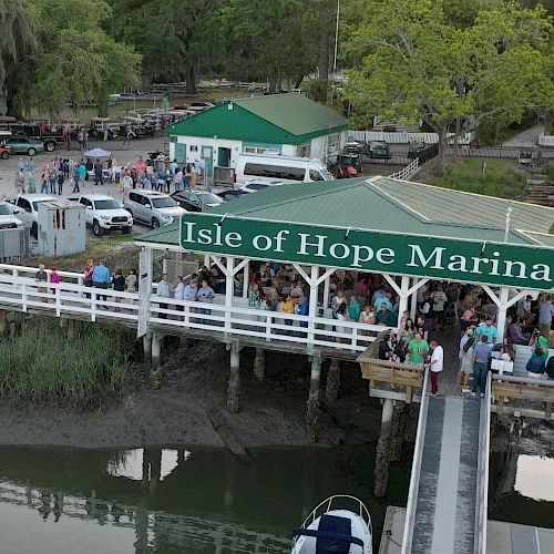 The image shows a crowd gathered at Isle of Hope Marina, with parked cars and greenery around, and water visible beneath the dock.