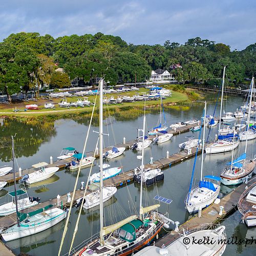 The image shows a marina with numerous boats docked, surrounded by greenery and houses in the background. © Kelli MIller Photography.