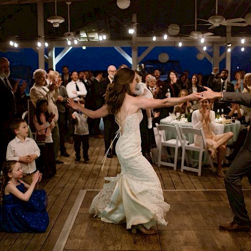 A newlywed couple dances in the center of a crowded event, with people around them watching and applauding.