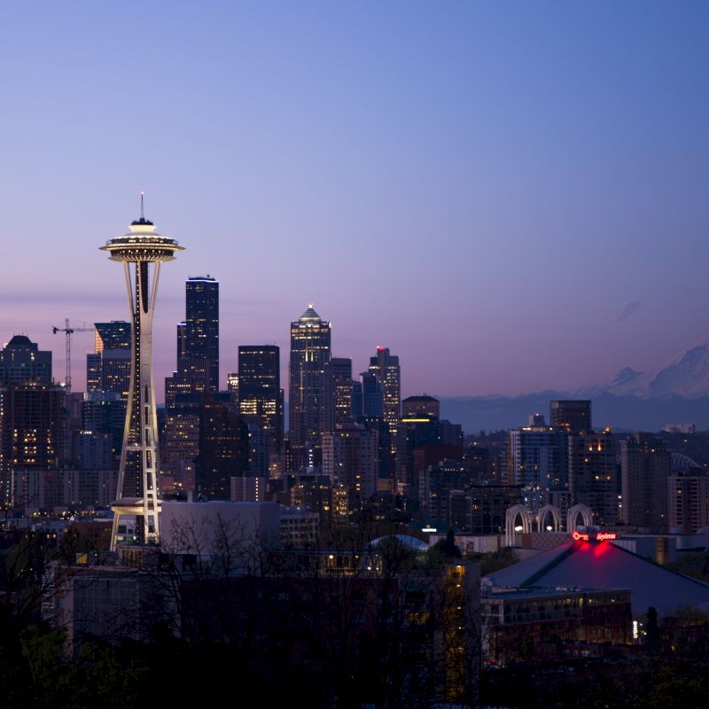 This image shows the Seattle skyline at dusk, with the Space Needle prominently visible, and Mount Rainier in the distant background.
