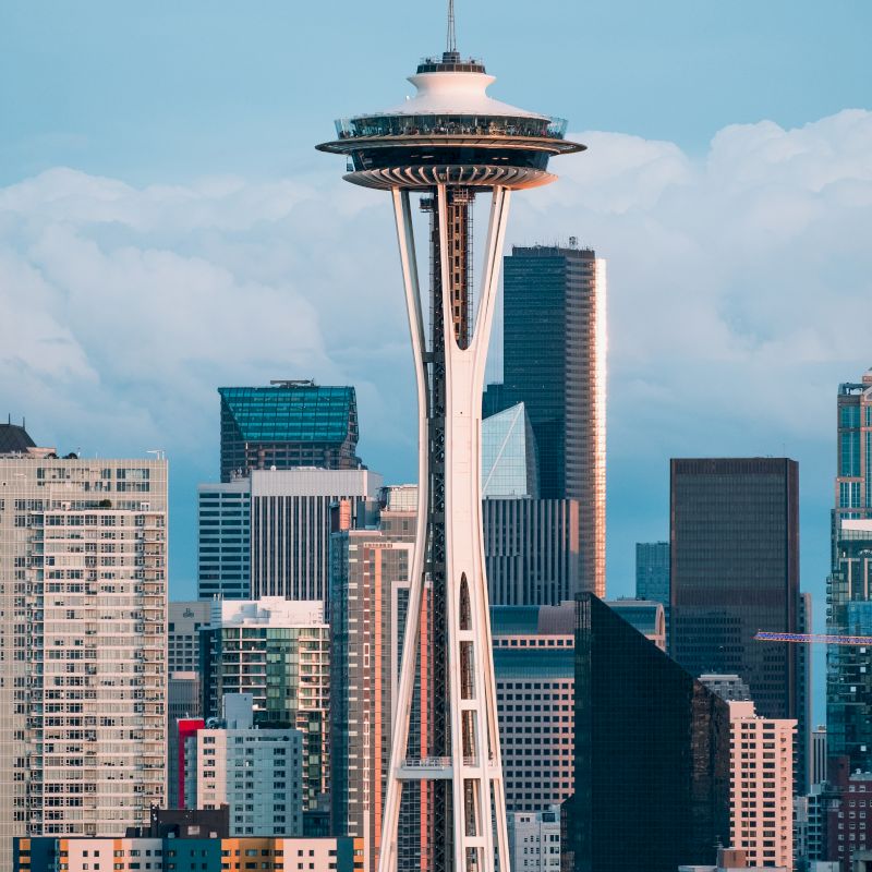 The image shows a city skyline dominated by a distinctive tower with a saucer-like top, likely the Space Needle, surrounded by various buildings.