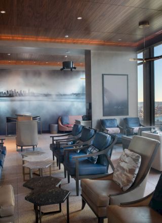 A modern lounge with ample seating, large windows overlooking a waterside view, and a mural on the wall depicting a city skyline ending the sentence.