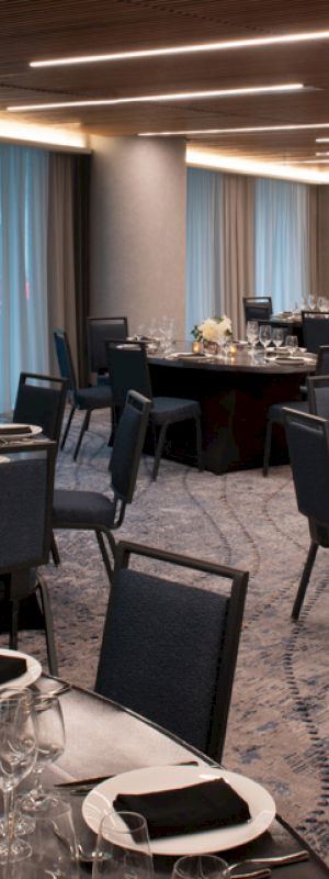 The image shows an elegantly set dining room with round tables, neatly arranged chairs, and decorative centerpieces placed on a patterned carpet.
