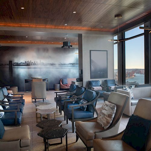 A modern lounge area with comfortable seating, a wall mural, large windows offering a waterfront view, and a Ferris wheel in the distance.