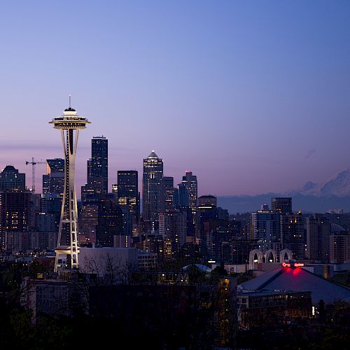 This image shows a city skyline at dusk, featuring a prominent tower and Mount Rainier in the background with a calming twilight hue.