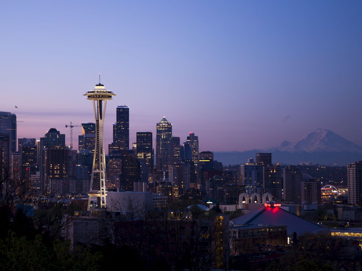 This image shows the Seattle skyline at dusk, featuring the Space Needle prominently, with Mount Rainier visible in the background.