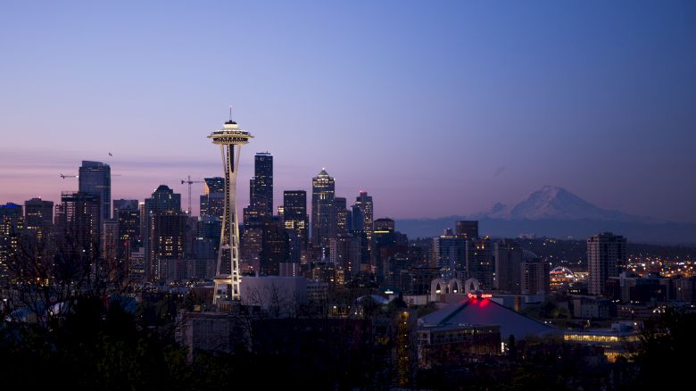 This image shows the Seattle skyline at dusk, featuring the Space Needle prominently, with Mount Rainier visible in the background.