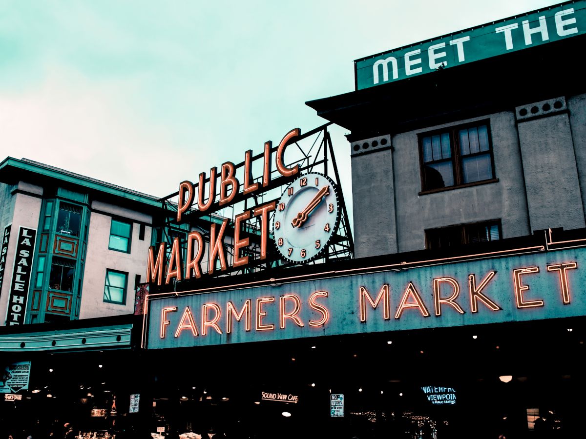 An iconic building featuring signs for "Public Market" and "Farmers Market" with a clock. Additional signs and buildings are in the backdrop.