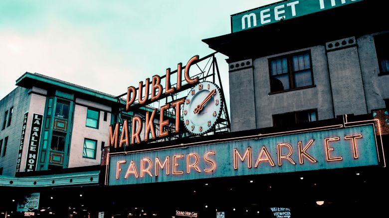 An iconic building featuring signs for "Public Market" and "Farmers Market" with a clock. Additional signs and buildings are in the backdrop.
